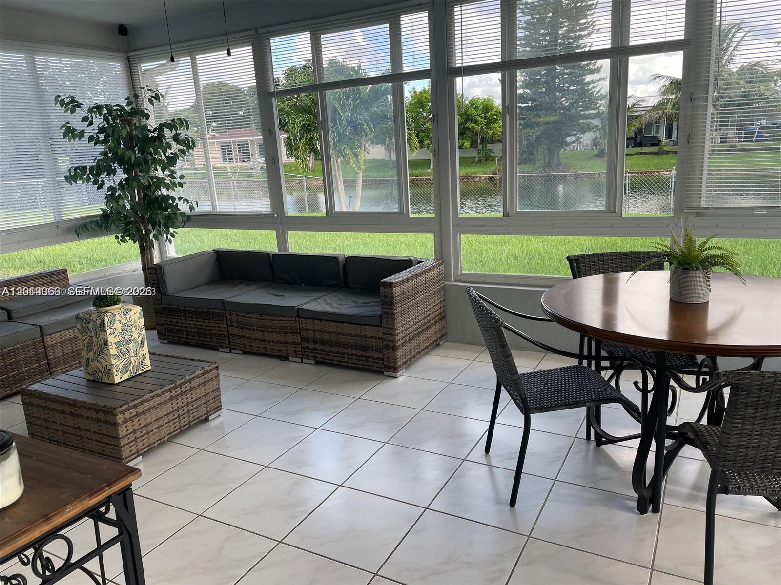 A sunroom features tile flooring, wicker furniture, and large windows overlooking a grassy yard — 9590 NW 24th Pl, Sunrise FL 33322, SUNRISE, FL