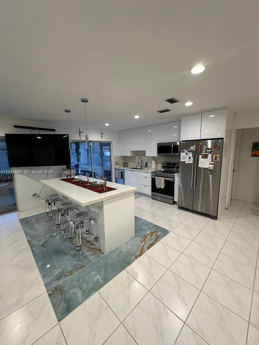 A modern kitchen features white cabinetry, stainless steel appliances, and a central island with stools — 9590 NW 24th Pl, Sunrise FL 33322, SUNRISE, FL