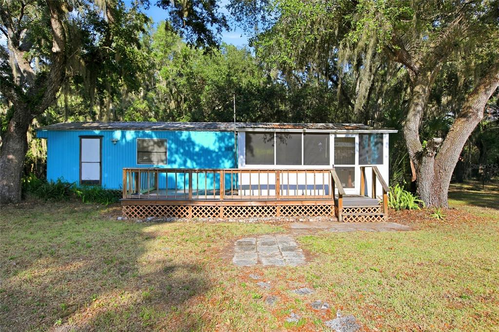 A blue mobile home features a wooden deck and a screened-in porch under large trees — 3348 OMEC STREET, LAKE WALES, FL