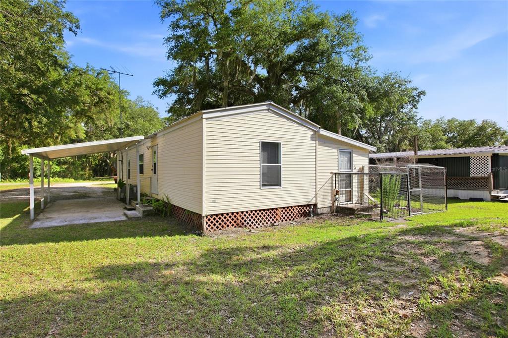 A light-colored mobile home features a side carport, lattice skirting, and a fenced-in yard area — 3348 OMEC STREET, LAKE WALES, FL