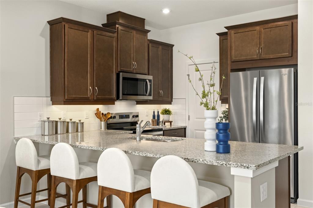 A kitchen features dark wood cabinets, granite countertops, a stainless steel refrigerator, and bar seating — 10031 GAZEBO ALLEY, ORLANDO, FL