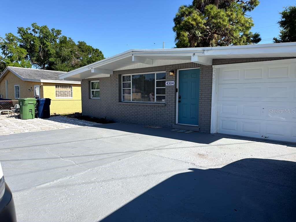 A single-story gray brick house features a blue front door and an attached garage — 4304 W ARCH STREET, TAMPA, FL