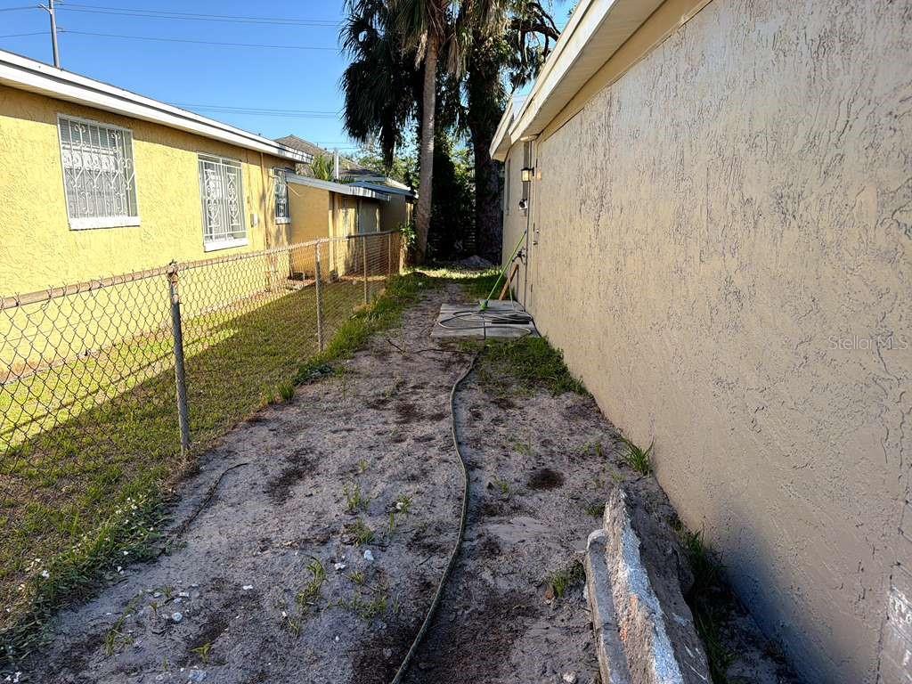 A narrow dirt side yard sits between a yellow house and a chain-link fence — 4304 W ARCH STREET, TAMPA, FL