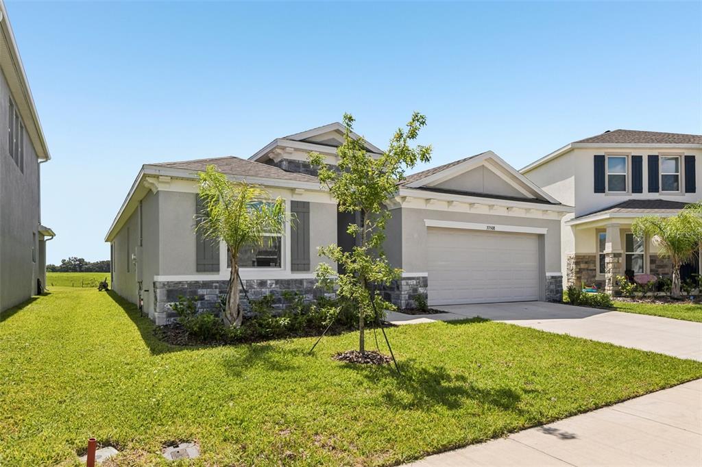 A single-story suburban house with a two-car garage, stone accents, and a grassy yard — 33508 DARLEY DALE TRAIL, WESLEY CHAPEL, FL