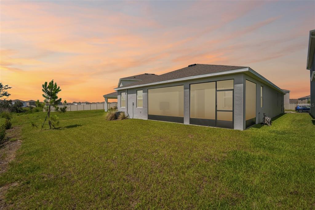 The exterior of a house features a screened-in patio and a grassy backyard at sunset — 33508 DARLEY DALE TRAIL, WESLEY CHAPEL, FL