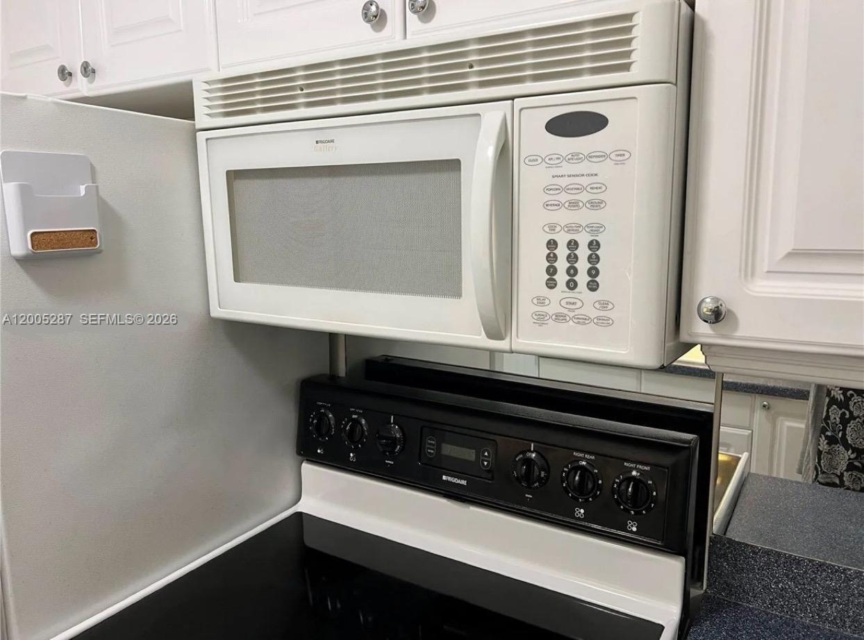 A white over-the-range microwave is mounted above a black electric stove in a kitchen — 500 Layne Blvd # 14, Hallandale Beach FL 33009, HALLANDALE BEACH, FL