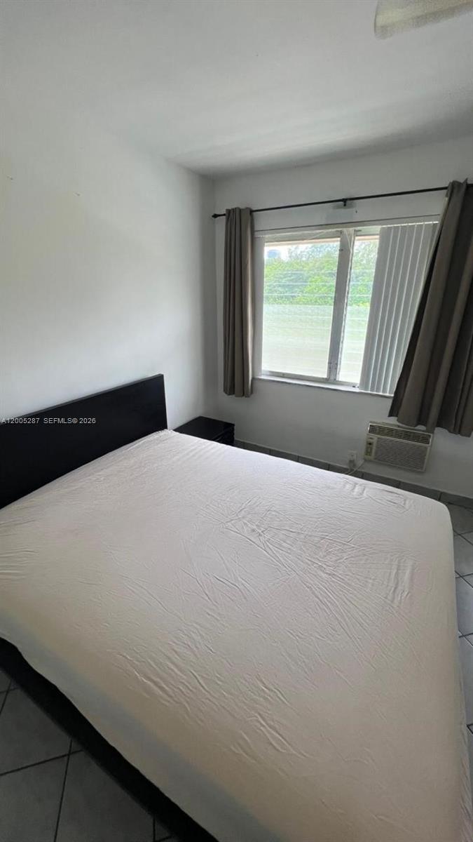 A bedroom features a bed with a black headboard, tile flooring, and a window with curtains — 500 Layne Blvd # 14, Hallandale Beach FL 33009, HALLANDALE BEACH, FL