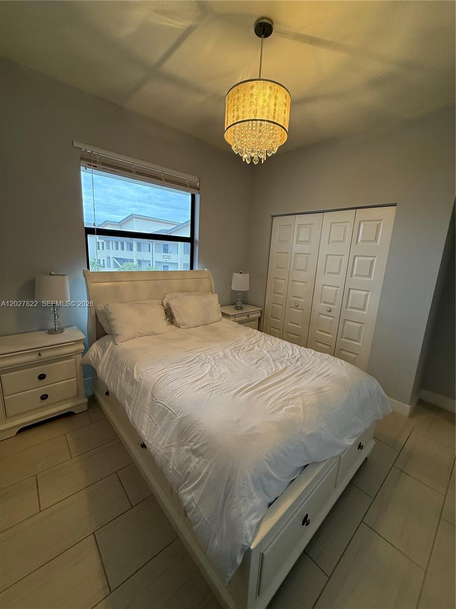 A bedroom features a white bed, matching nightstands, a crystal chandelier, and a closet — 7815 NW 104th Ave # 32, Doral FL 33178, DORAL, FL
