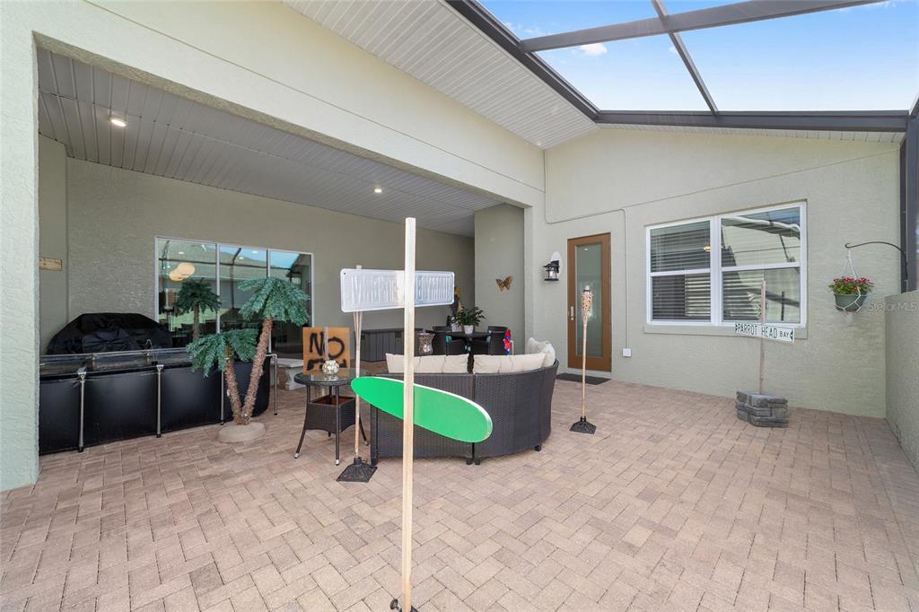 A covered patio features paver flooring, outdoor furniture, and decorative street signs under a screen enclosure — 8780 SW 93RD CIRCLE, OCALA, FL