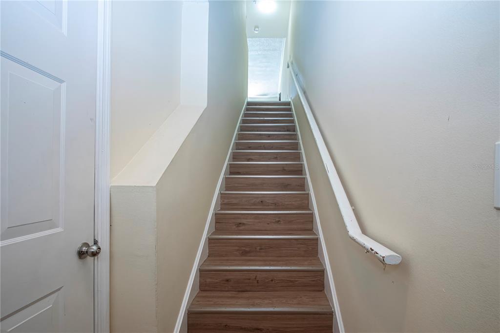 A staircase with wood-look treads leads upward between two beige walls with a handrail — 5711 BENTGRASS DRIVE UNIT 19-202, SARASOTA, FL