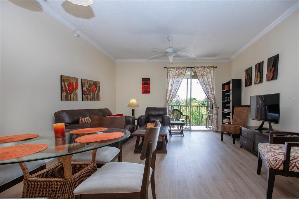 A living and dining area features wood-look flooring, a glass table, and a balcony view — 5711 BENTGRASS DRIVE UNIT 19-202, SARASOTA, FL