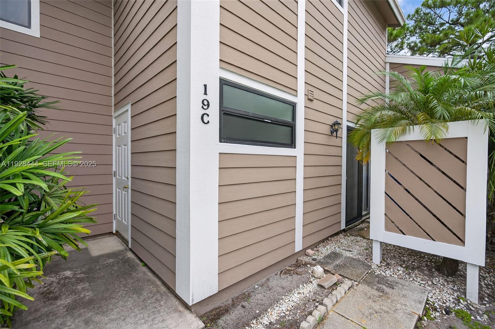 The exterior of a tan, two-story townhouse features a white-trimmed door and a privacy screen — 707 Stonewood Ct # 19C, Jupiter FL 33458, JUPITER, FL