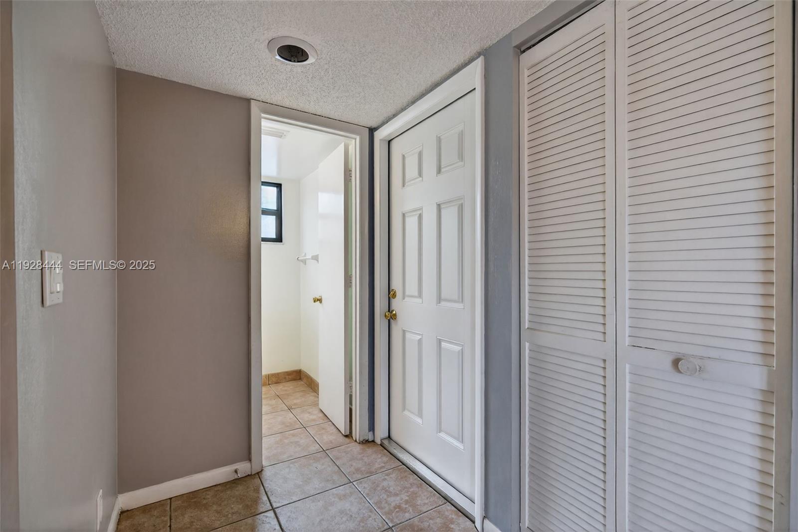 A hallway features tiled floors, a white door, louvered closet doors, and an open doorway — 707 Stonewood Ct # 19C, Jupiter FL 33458, JUPITER, FL