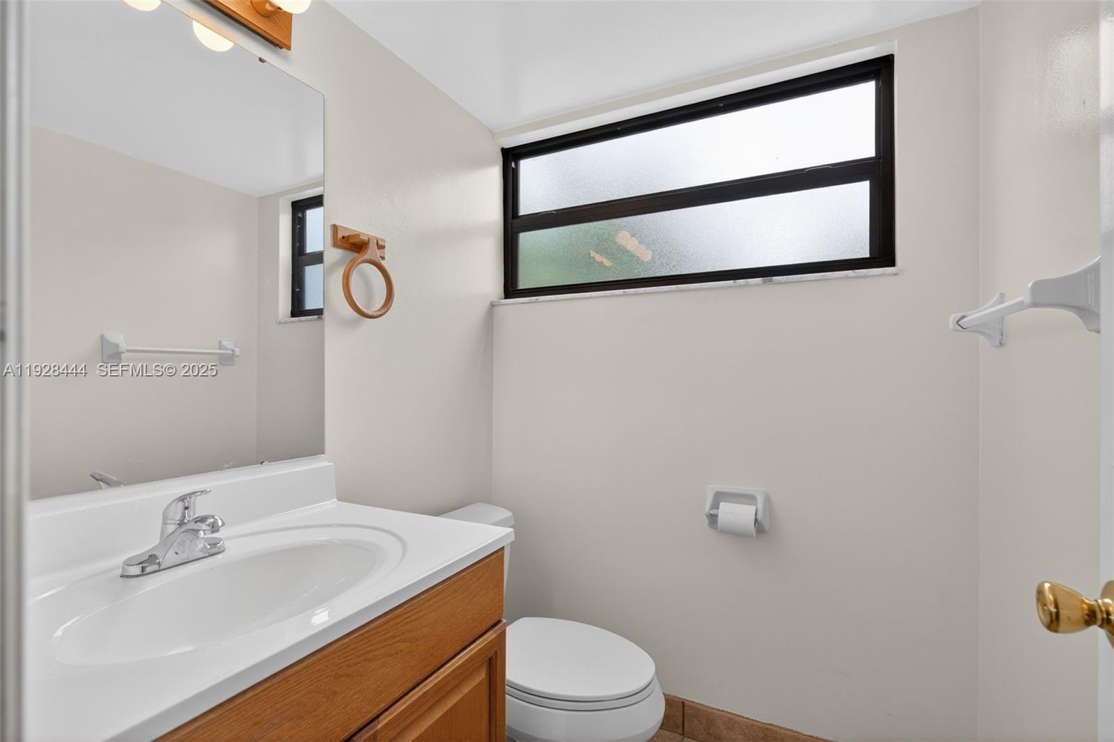 A bathroom features a wooden vanity, a white sink, a toilet, and a frosted window — 707 Stonewood Ct # 19C, Jupiter FL 33458, JUPITER, FL