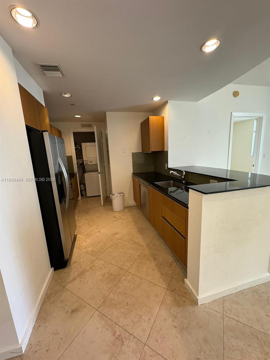 A kitchen features wood cabinets, black countertops, stainless steel appliances, and tile flooring — 1060 BRICKELL AV # 2603, Miami FL 33131, MIAMI, FL