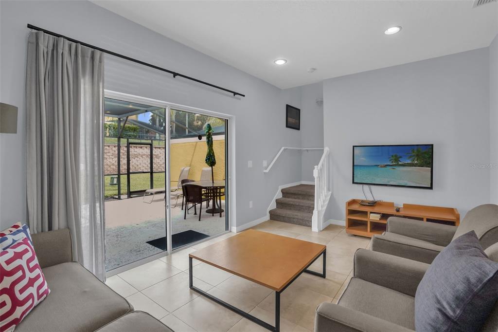 A living room with tile floors, a sliding glass door, and stairs leading upward — 3043 WHITE ORCHID ROAD, KISSIMMEE, FL