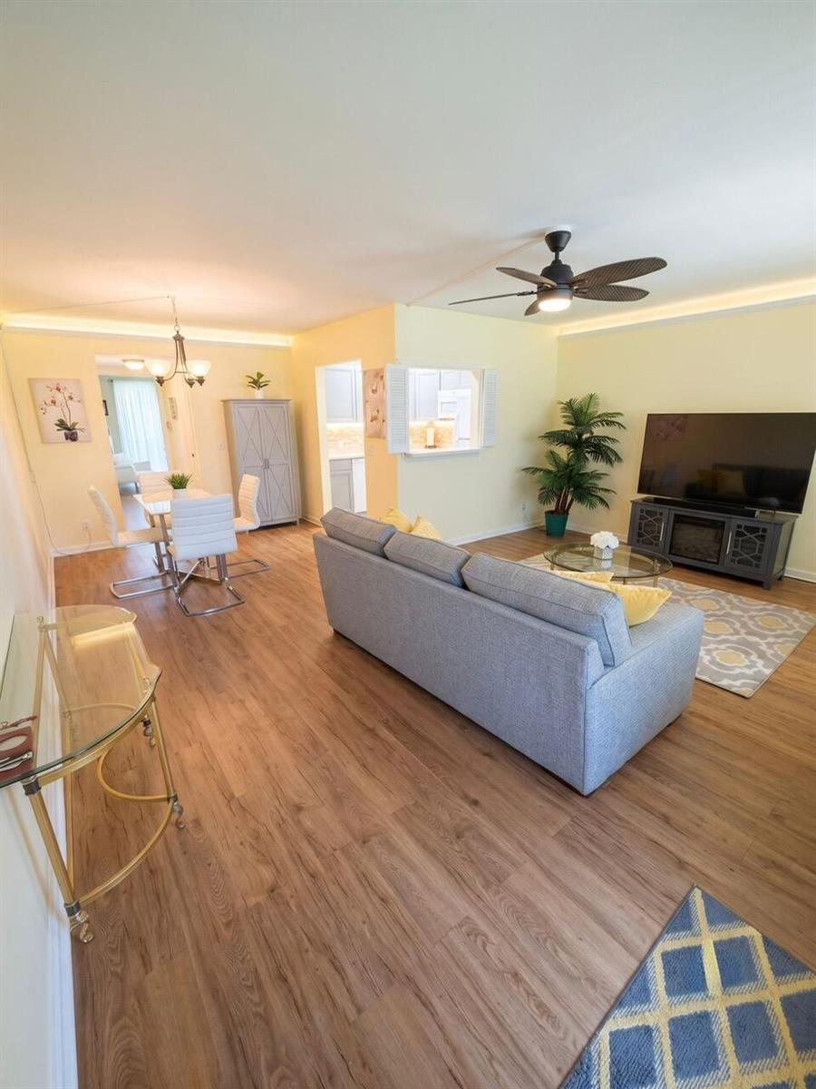 A living room and dining area with light wood flooring, a grey sofa, and ceiling fan — 68 Brighton B, Boca Raton FL 33434, BOCA RATON, FL