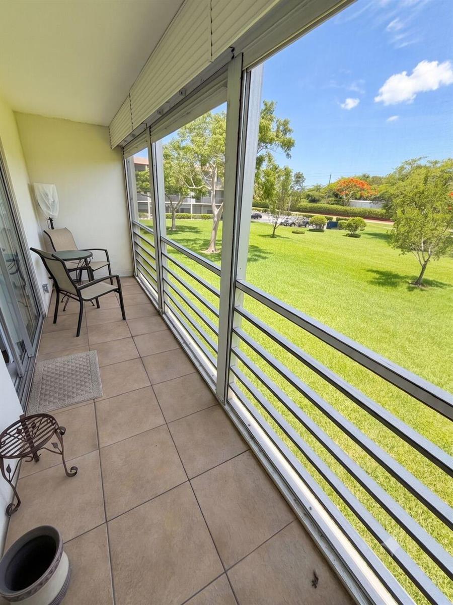 A screened-in balcony features tiled flooring, patio furniture, and a view of a grassy lawn — 68 Brighton B, Boca Raton FL 33434, BOCA RATON, FL