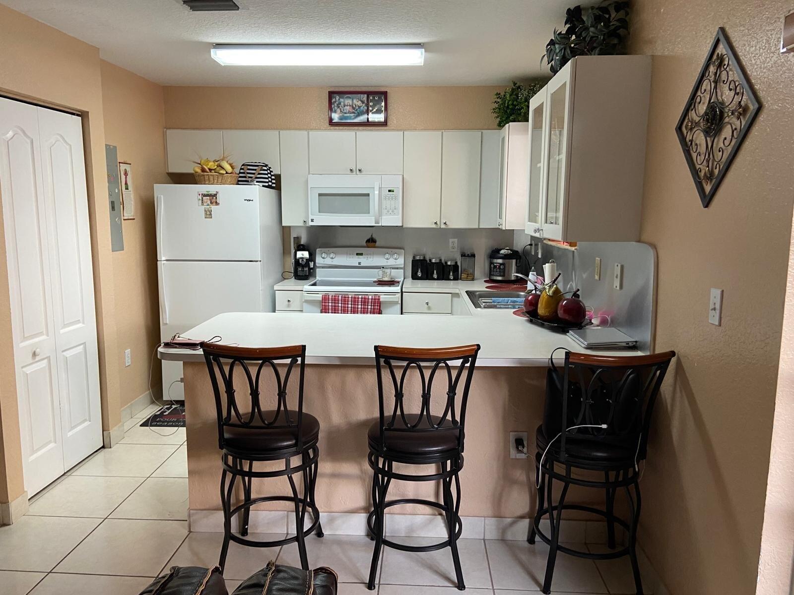 A kitchen features white cabinetry, a breakfast bar with three stools, and light-colored tile flooring — 8752 NW 107th Terrace # 8752, Hialeah Gardens FL 33018, HIALEAH GARDENS, FL