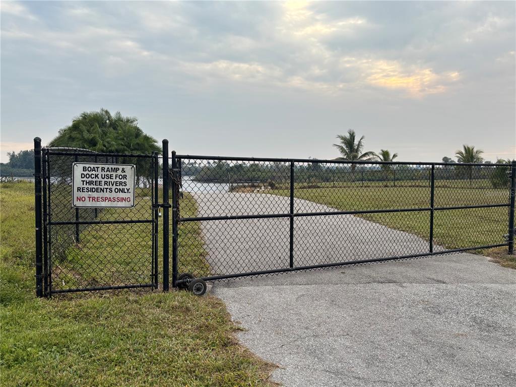 A black chain-link gate blocks a paved driveway leading toward a body of water — 31083 PEACE STREET, PUNTA GORDA, FL