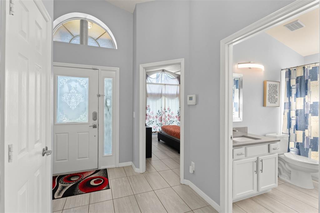 An entryway with tile flooring, a front door with a transom window, and an adjacent bathroom — 8060 SANTEE DRIVE, KISSIMMEE, FL