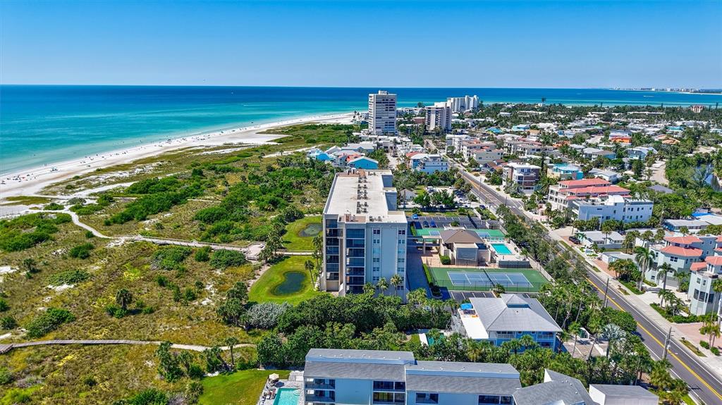 An aerial view shows a multi-story apartment building with tennis courts near a sandy beach — 420 BEACH ROAD UNIT 508, SARASOTA, FL