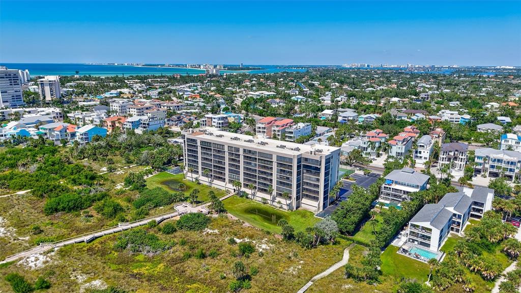 An aerial view shows a tall residential building with tennis courts near a sandy beach — 420 BEACH ROAD UNIT 508, SARASOTA, FL
