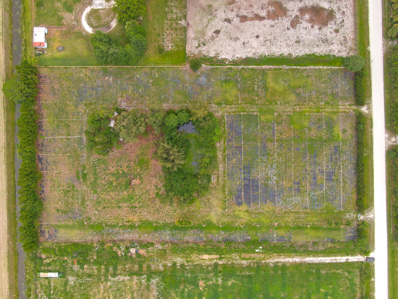 An aerial view of a rectangular plot of land featuring a central pond and trees — 16295 Rustic Road, Wellington FL 33470, WELLINGTON, FL