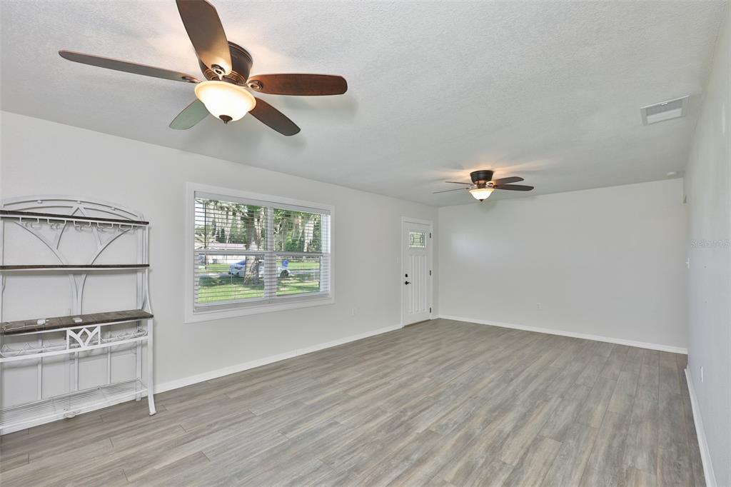A living room with light gray walls, wood-look flooring, two ceiling fans, and a window — 4306 STRAUSS ROAD, PLANT CITY, FL
