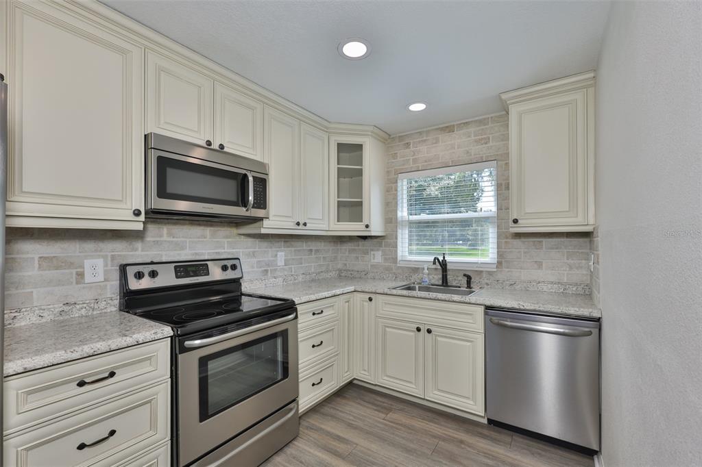 A kitchen with cream cabinets, stainless steel appliances, granite countertops, and a brick-style backsplash — 4306 STRAUSS ROAD, PLANT CITY, FL