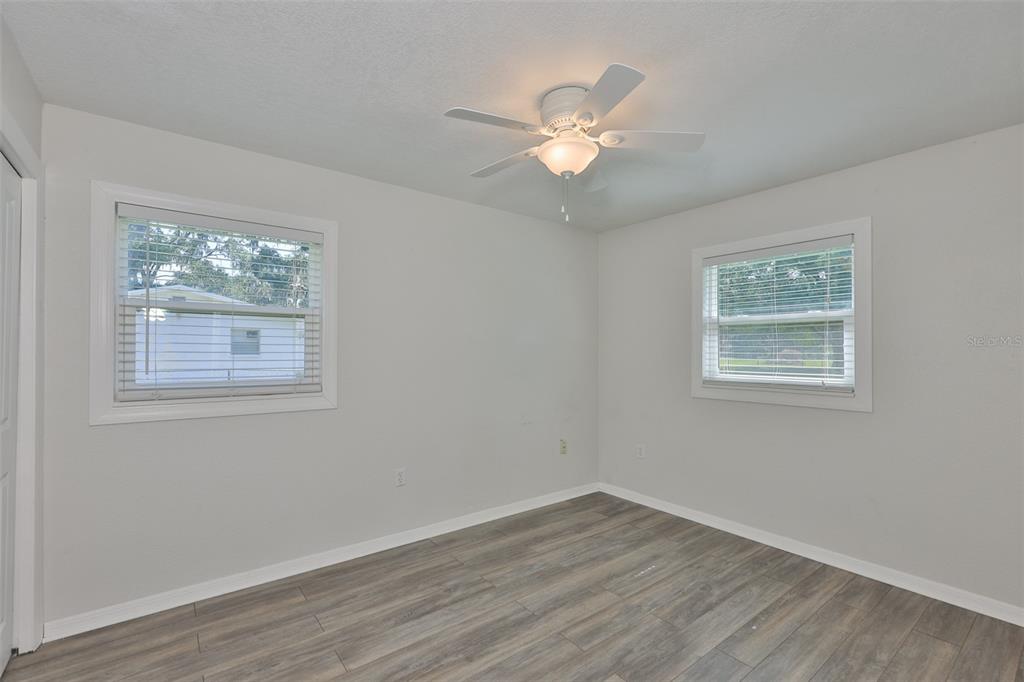 An empty bedroom features light gray walls, wood-look flooring, two windows, and a ceiling fan — 4306 STRAUSS ROAD, PLANT CITY, FL