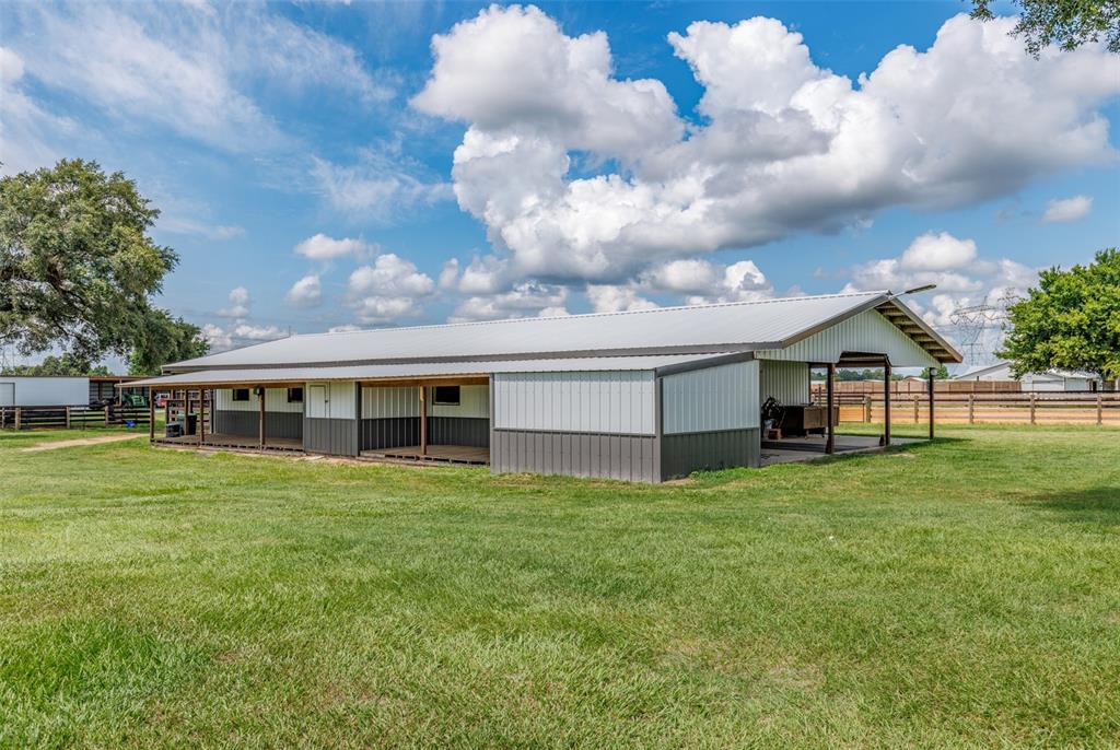 A metal-sided barn with a covered porch sits in a grassy field under a cloudy sky — 1285 NW 102ND BOULEVARD, WILDWOOD, FL