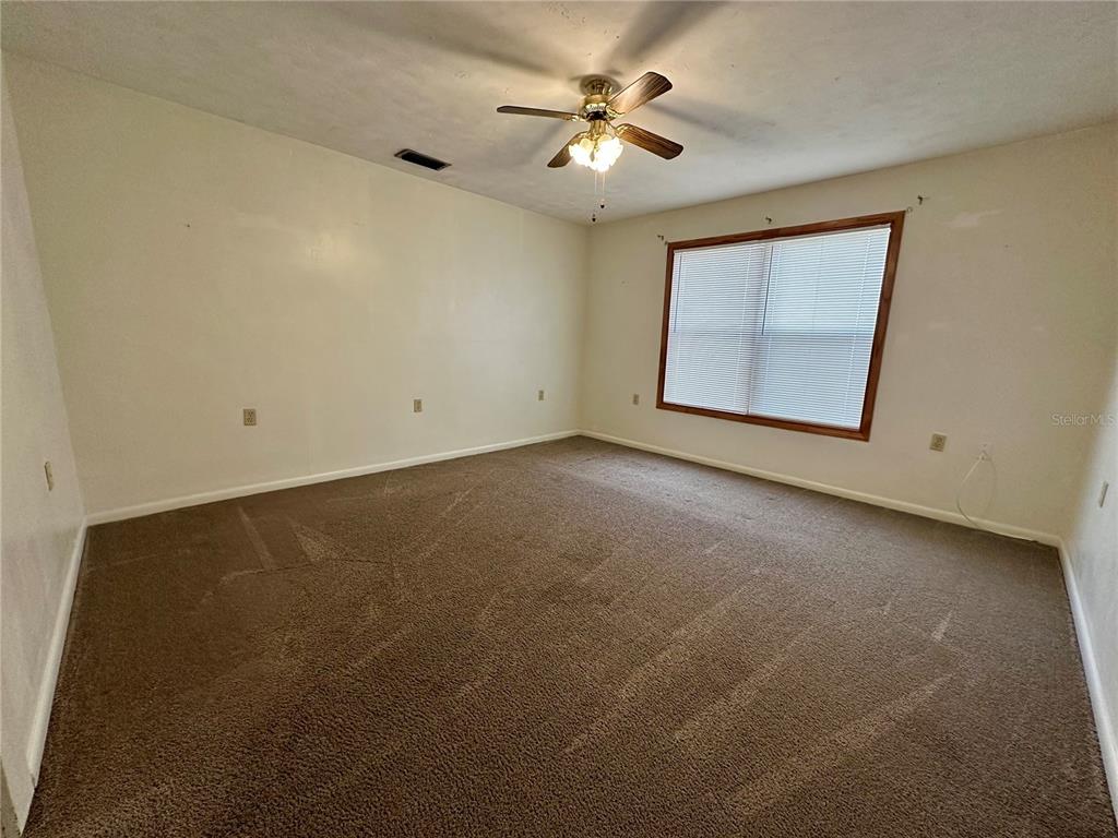 An empty bedroom features beige walls, brown carpeting, a ceiling fan, and a single window — 520 SW 5TH AVENUE, LAKE BUTLER, FL