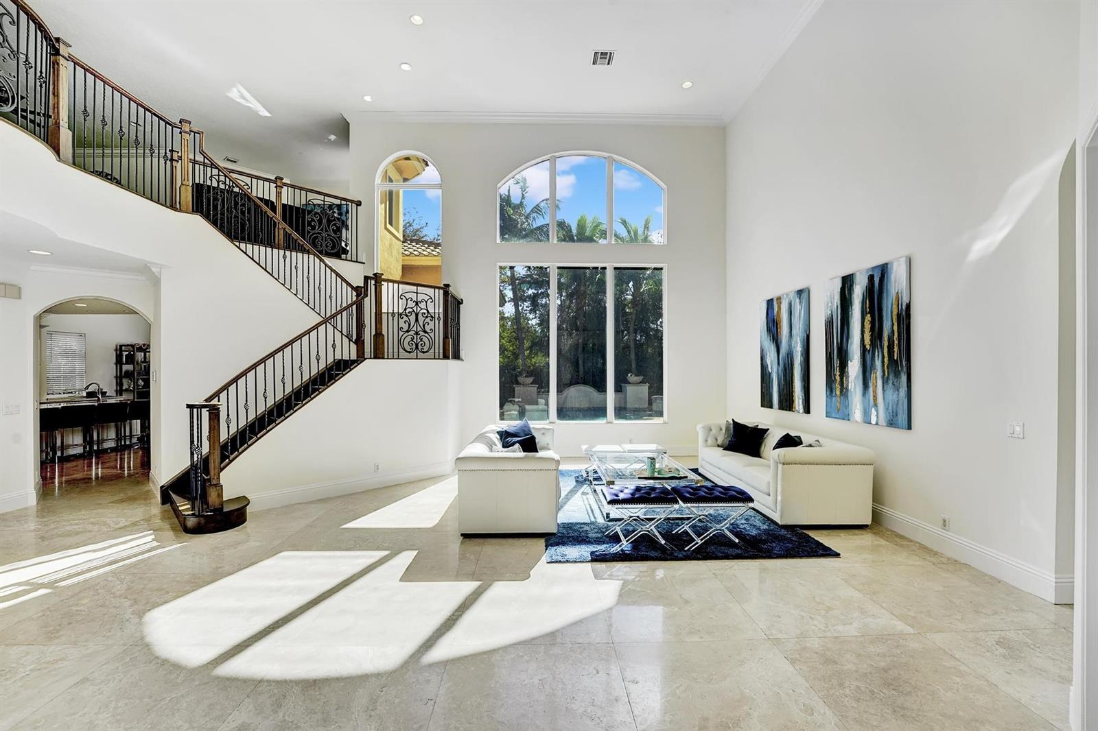 A spacious living room features a grand staircase, high ceilings, large windows, and tile flooring — 43 Coconut Lane, Ocean Ridge FL 33435, OCEAN RIDGE, FL