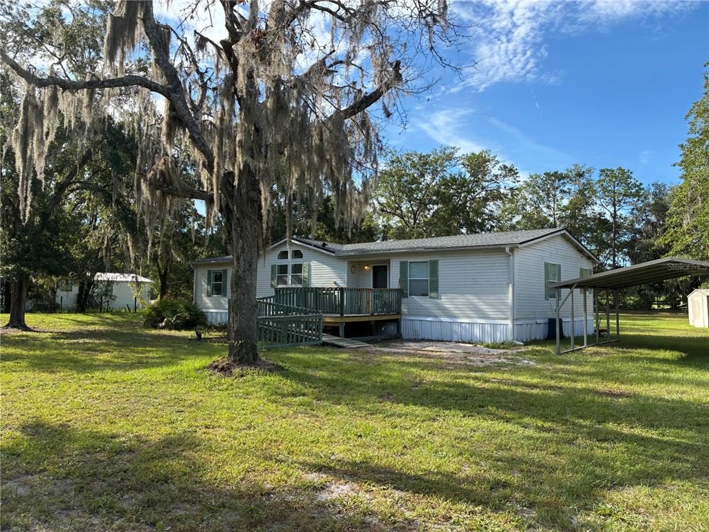 A single-story manufactured home features a wooden deck with a ramp and a carport — 21919 NE 69TH PLACE, MELROSE, FL