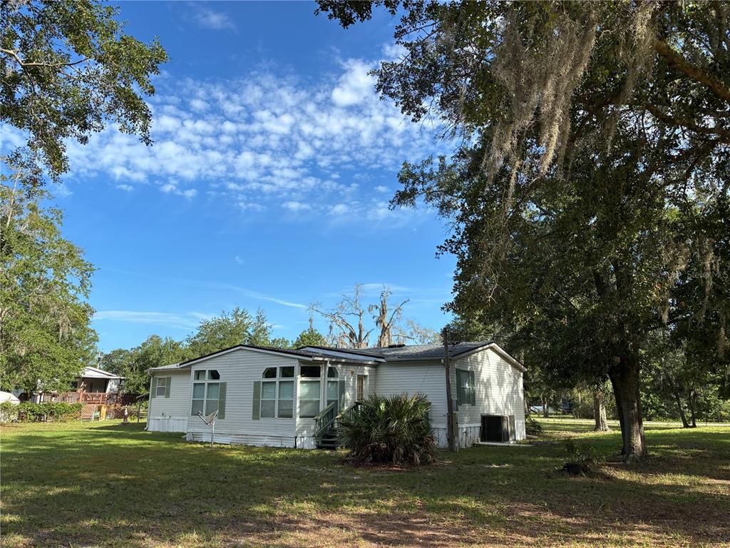 A single-story manufactured home sits on a grassy lot surrounded by large, moss-draped trees — 21919 NE 69TH PLACE, MELROSE, FL