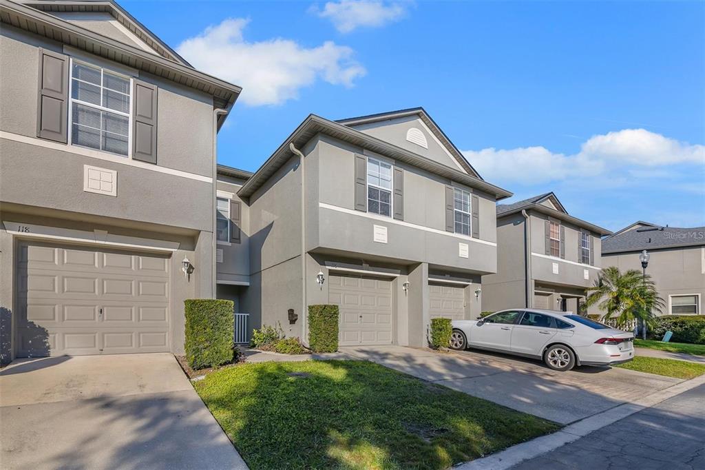 A row of grey two-story townhouses with attached garages and concrete driveways under a blue sky — 116 PHILADELPHIA WAY, WINTER SPRINGS, FL
