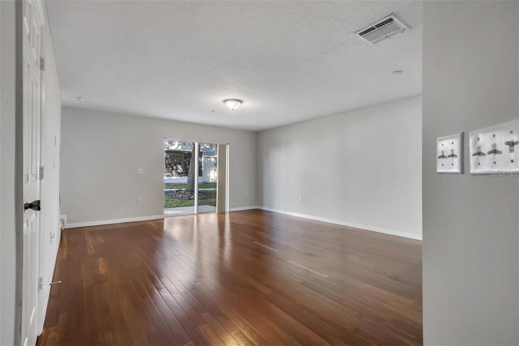 An empty living room with hardwood floors, white walls, and a sliding glass door — 116 PHILADELPHIA WAY, WINTER SPRINGS, FL