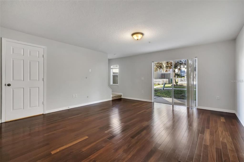 An empty living room features dark wood flooring, light gray walls, and a sliding glass door — 116 PHILADELPHIA WAY, WINTER SPRINGS, FL