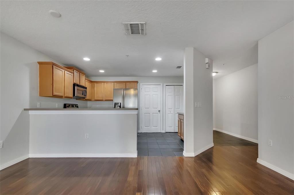 A kitchen with light wood cabinets and stainless steel appliances overlooks a hardwood-floored living area — 116 PHILADELPHIA WAY, WINTER SPRINGS, FL