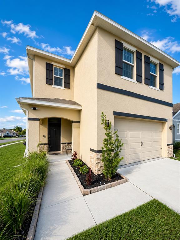 A two-story tan stucco house features a front-facing garage and a covered entryway — 32649 PEZ LANDING LANE, WESLEY CHAPEL, FL