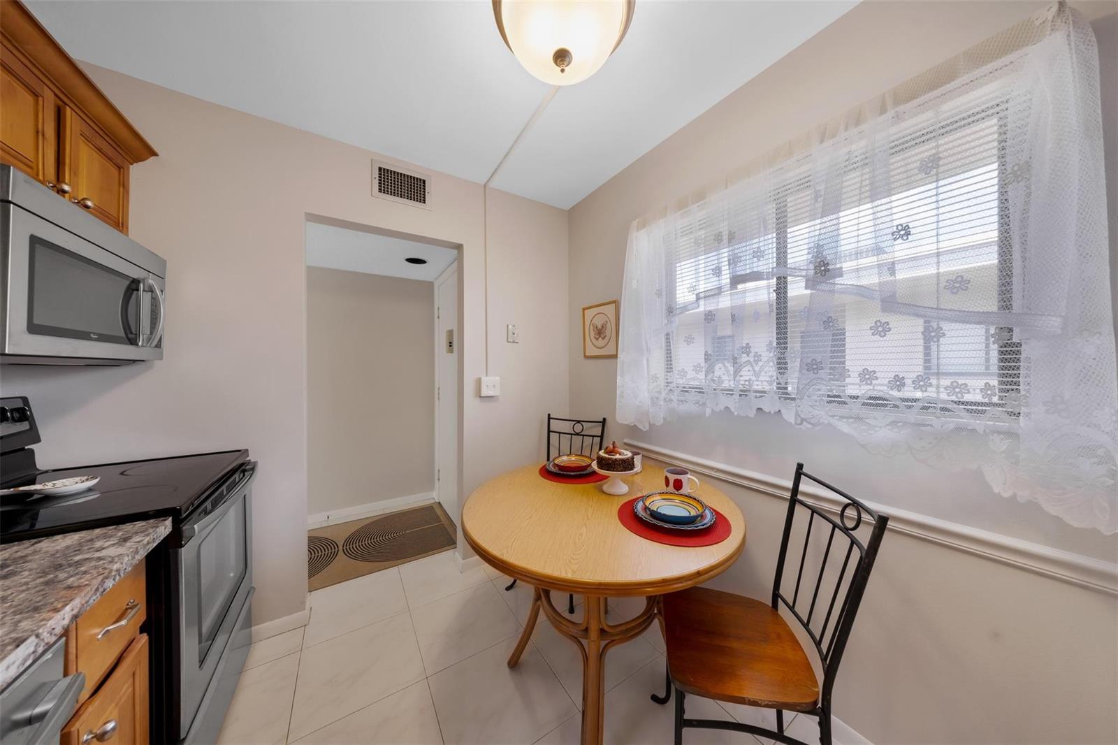 A small kitchen features a round wooden dining table, light tile floors, and wooden cabinets — 5250 Las Verdes Circle # 317, Delray Beach FL 33484, DELRAY BEACH, FL