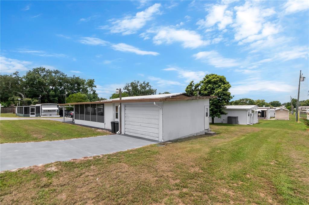 A white house with a garage and a screened-in porch sits on a grassy lot — 39219 OLA AVENUE, ZEPHYRHILLS, FL