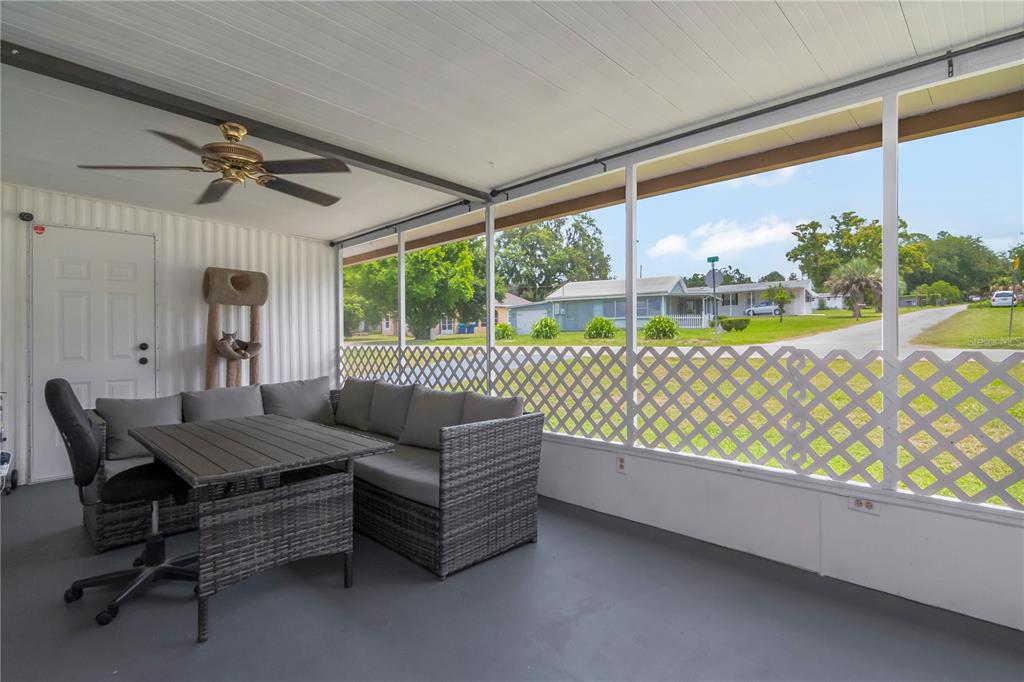 A screened-in porch features gray wicker furniture, a ceiling fan, and a view of neighborhood homes — 39219 OLA AVENUE, ZEPHYRHILLS, FL