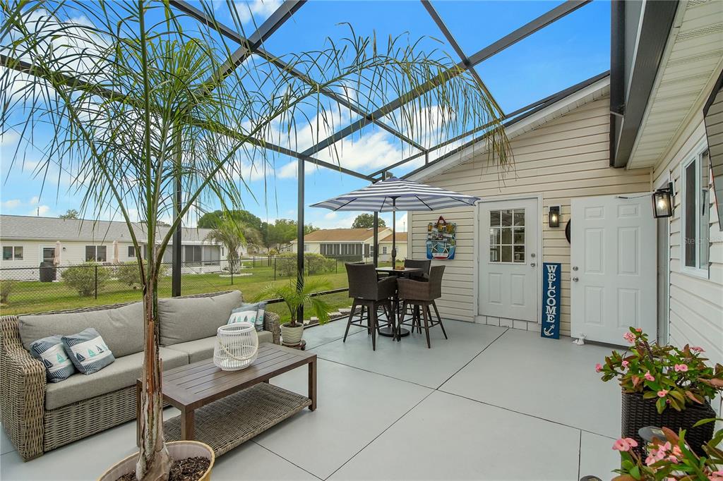 A screened-in patio features a wicker sofa, a dining set with an umbrella, and potted plants — 10608 SE 174TH LOOP, SUMMERFIELD, FL
