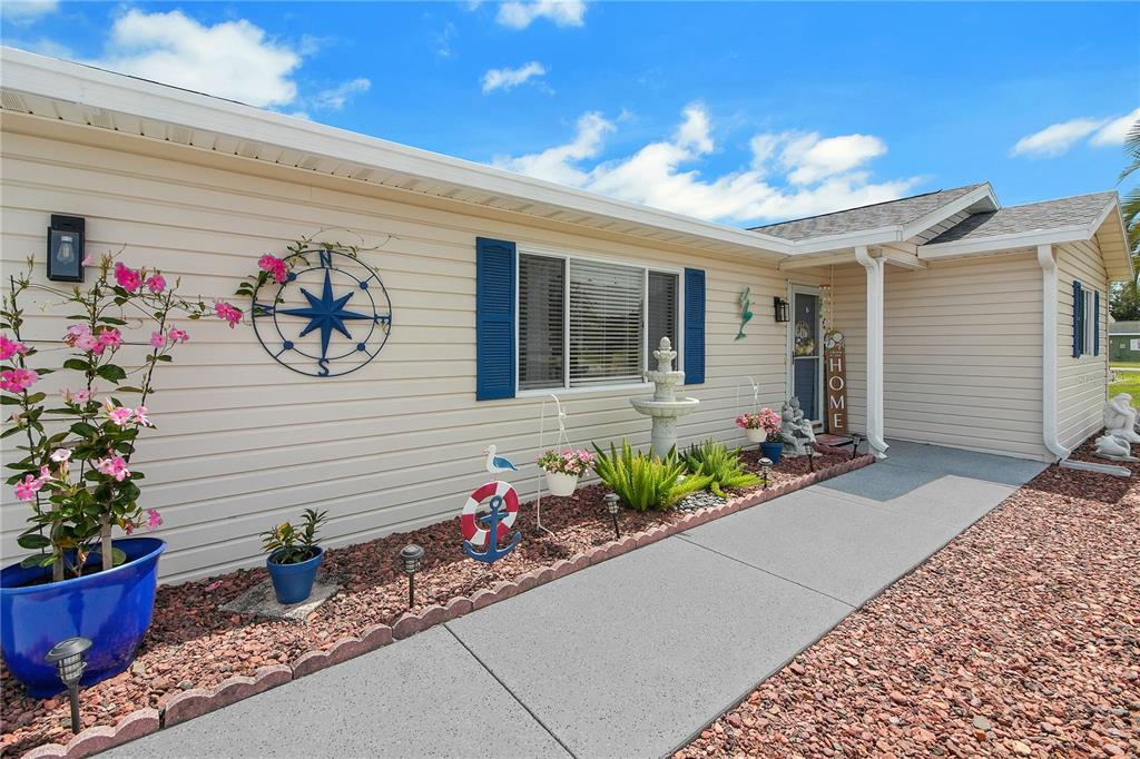 A light-colored house exterior features a concrete walkway, a compass wall decoration, and a fountain — 10608 SE 174TH LOOP, SUMMERFIELD, FL