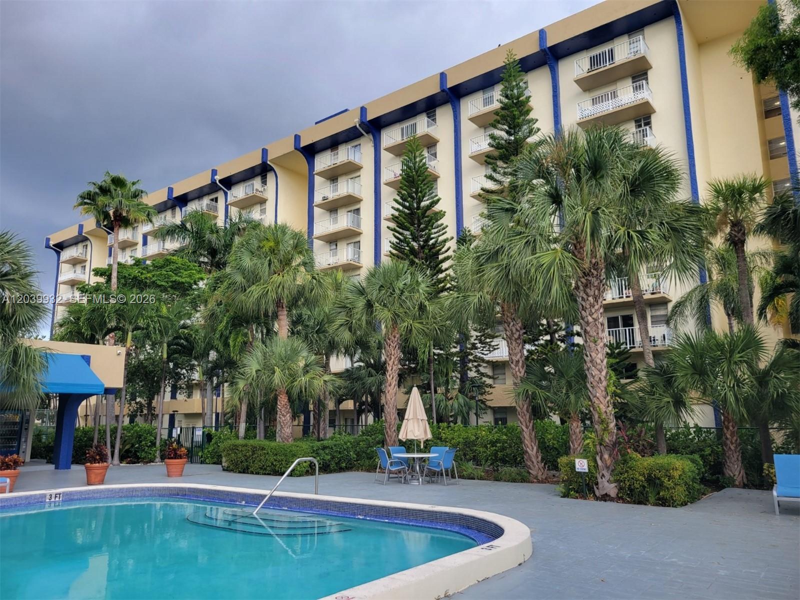 A multi-story apartment building with blue accents stands behind a swimming pool and palm trees — 4550 NW 9th St # 512E, Miami FL 33126, MIAMI, FL
