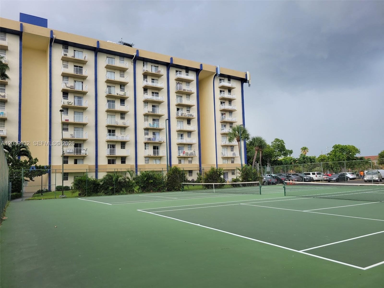 A multi-story apartment building stands behind a green tennis court under a cloudy sky — 4550 NW 9th St # 512E, Miami FL 33126, MIAMI, FL