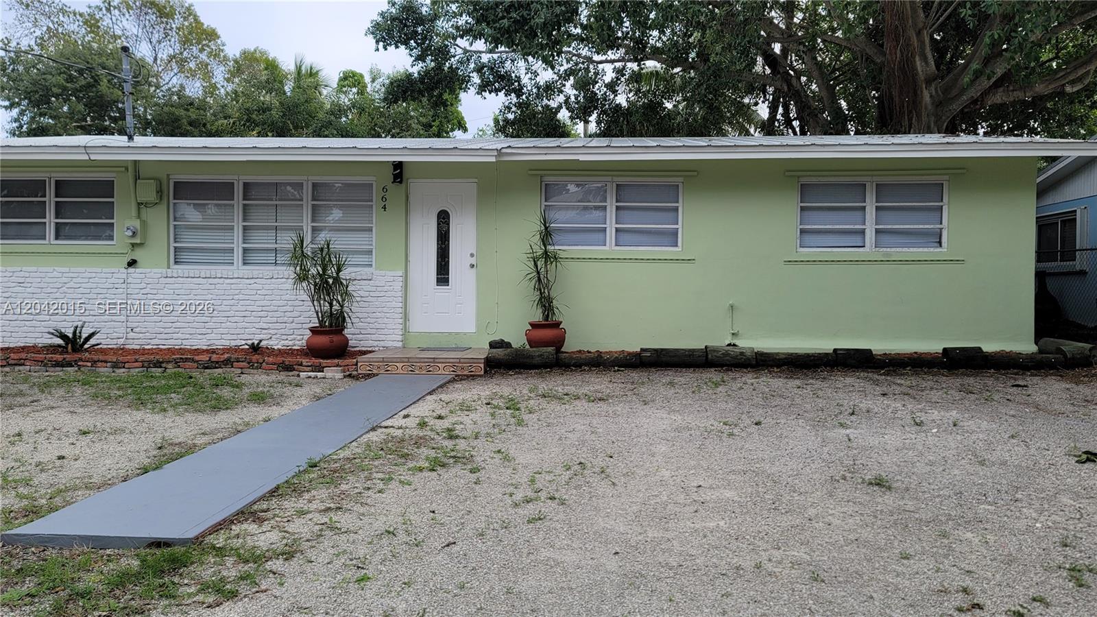 A single-story house with light green siding, a white front door, and a gravel yard — 664 Colson Dr, Key Colony FL 33037, KEY COLONY, FL