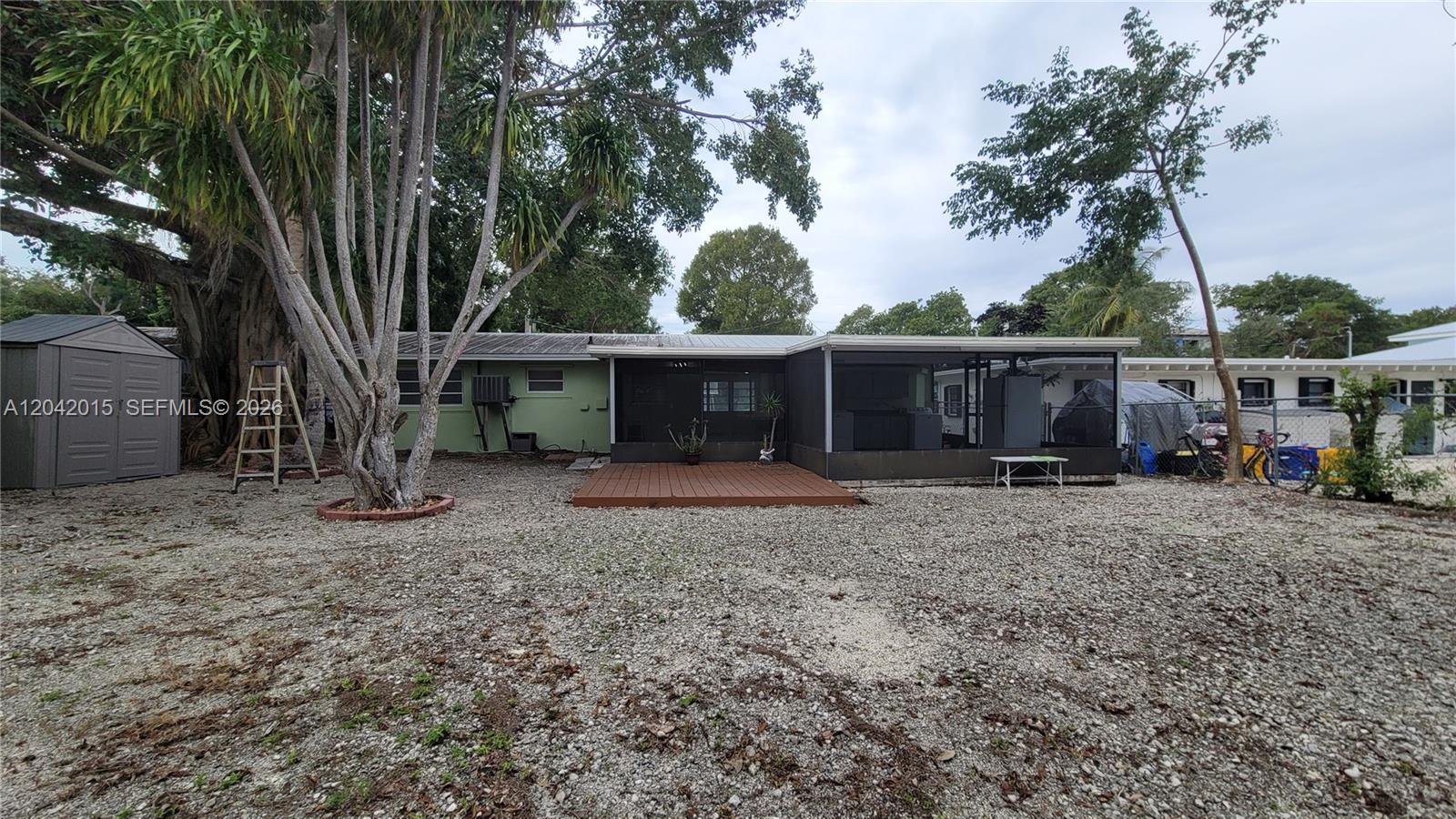 A gravel backyard features a wooden deck, a screened-in porch, and a storage shed — 664 Colson Dr, Key Colony FL 33037, KEY COLONY, FL